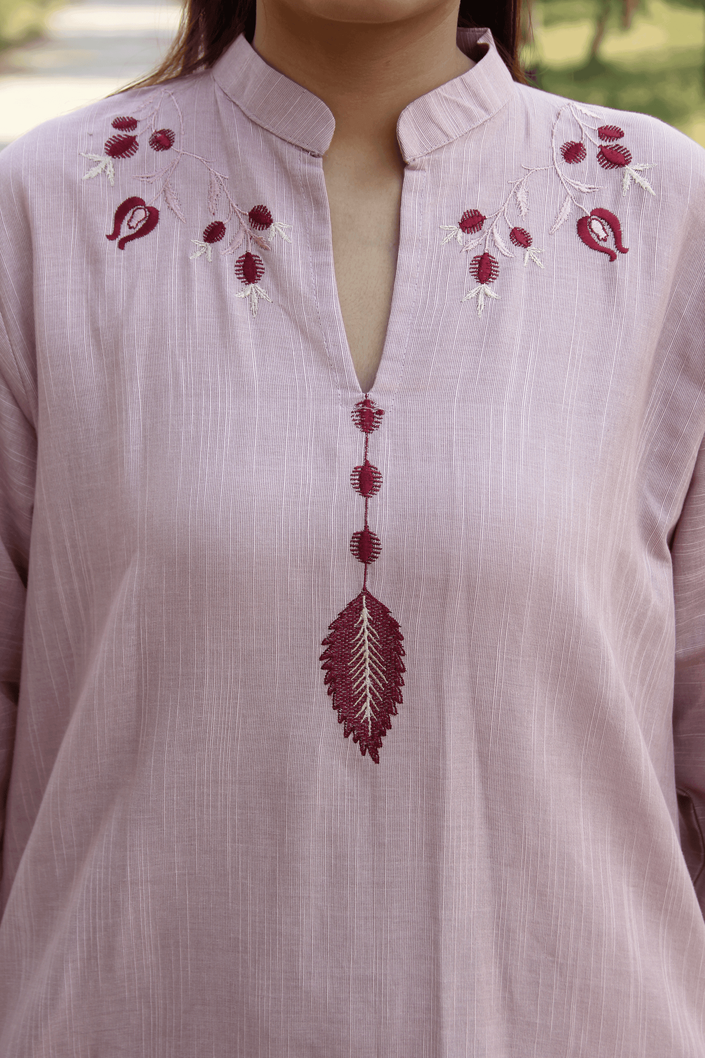 Light pink shirt with red floral embroidery on a blurred natural background