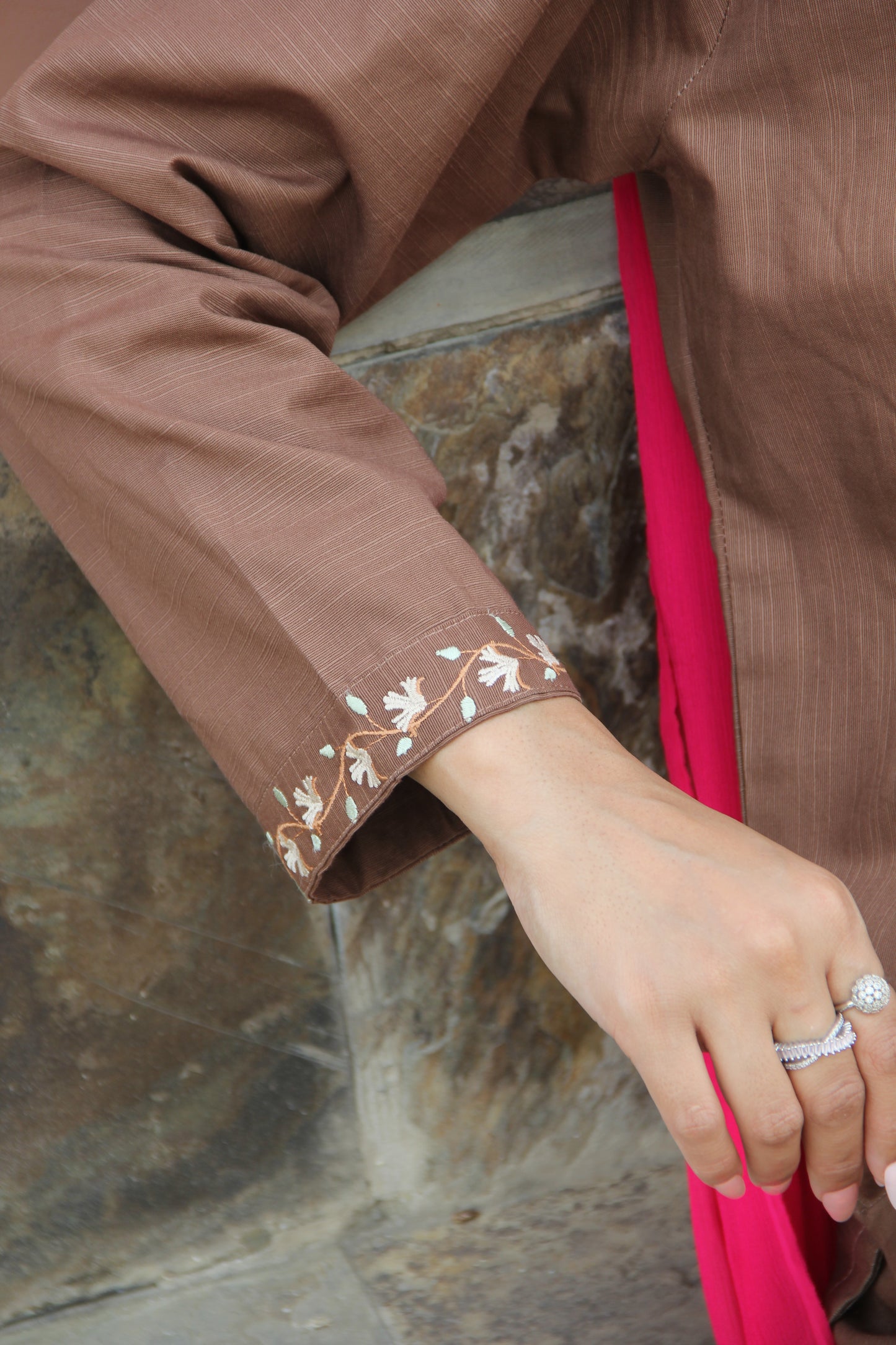Close-up of a hand wearing a ring on a brown garment with floral embroidery.