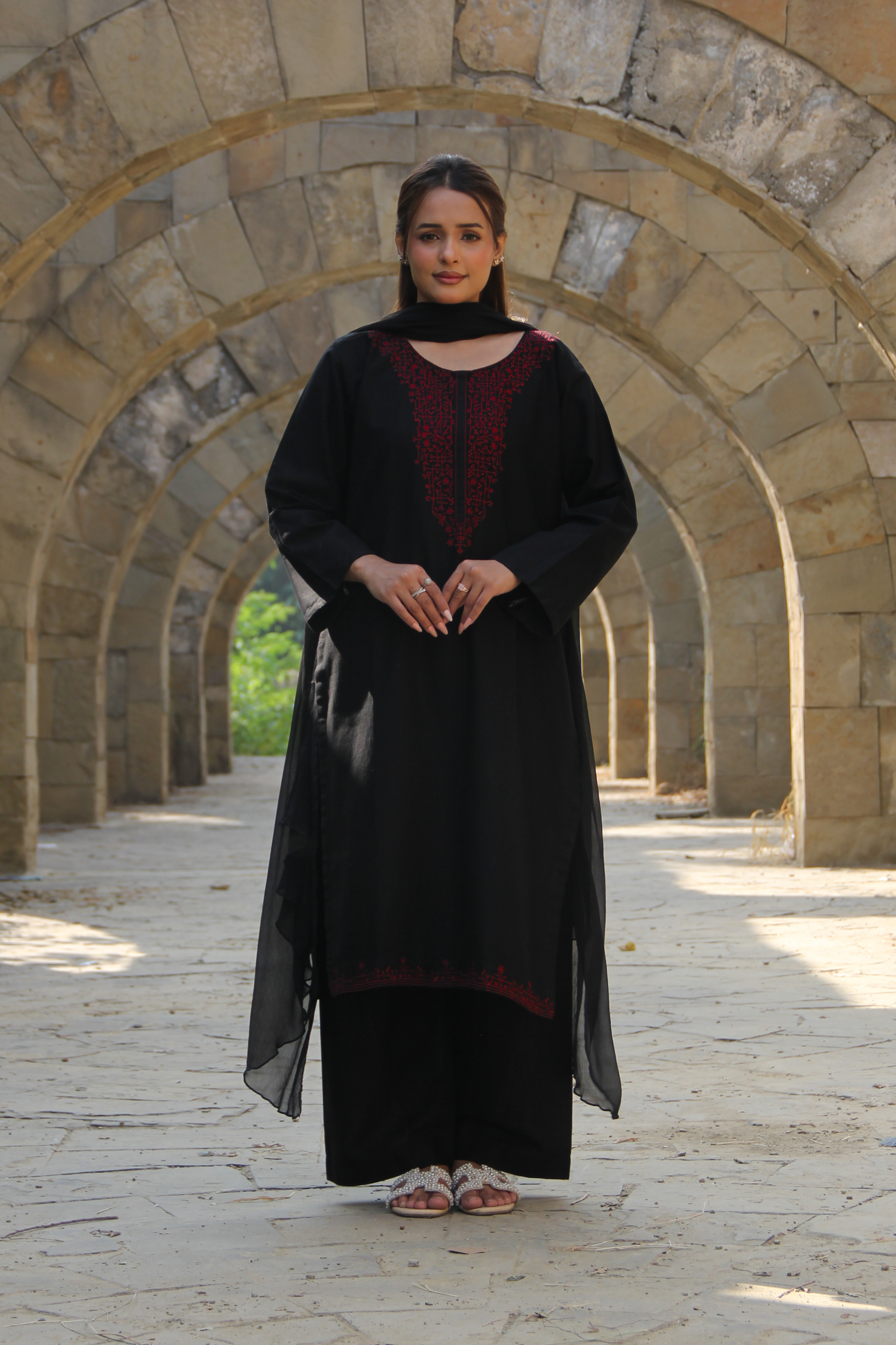 Woman in a black dress standing in front of stone arches