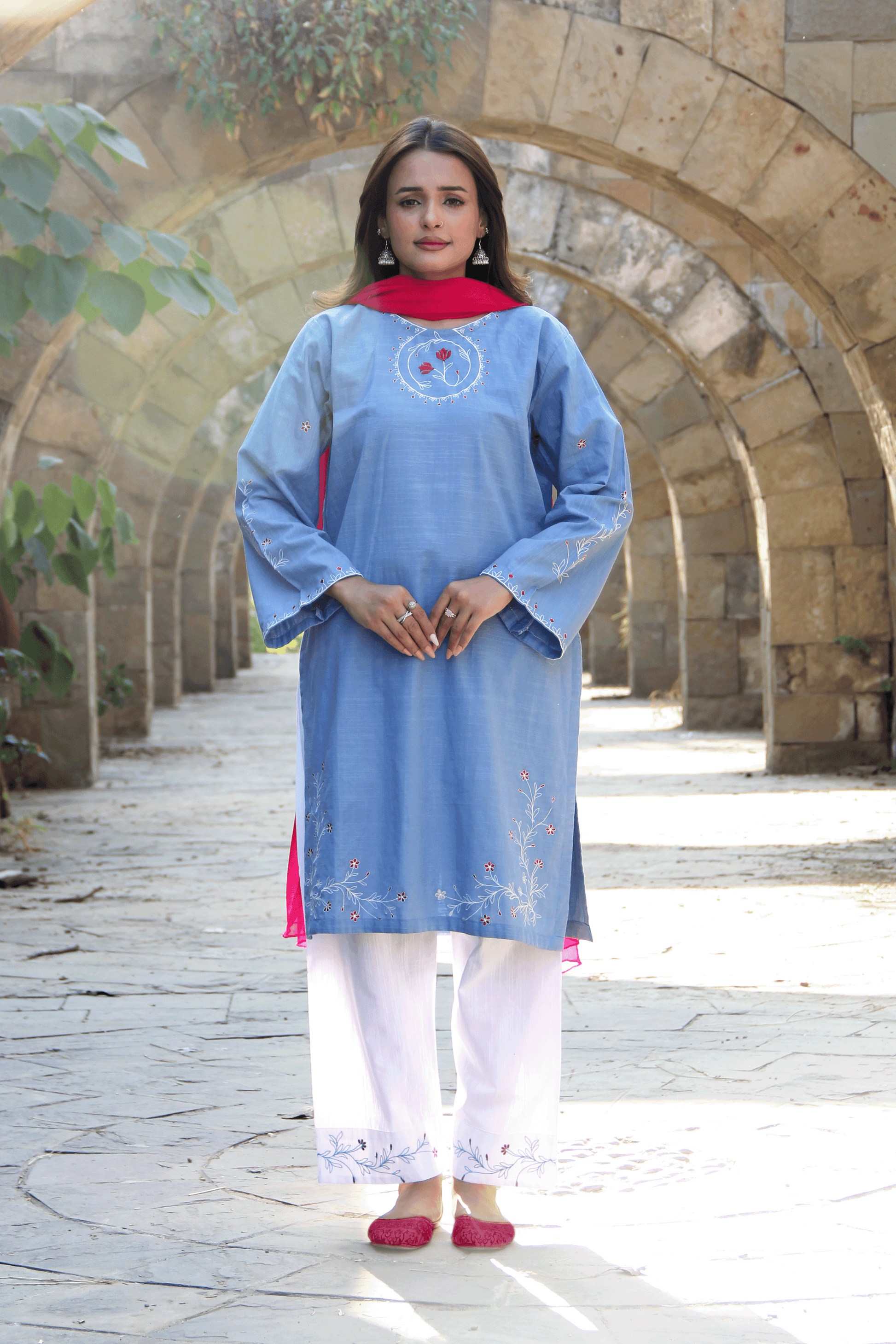 Woman in a light blue kurta with white pants standing in front of stone arches.