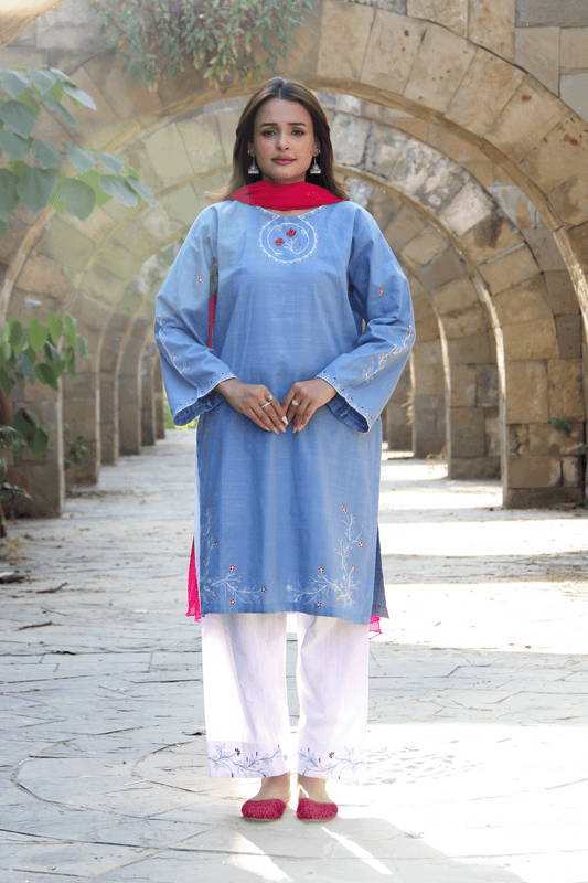 Woman in a light blue kurta with white pants standing in front of stone arches.