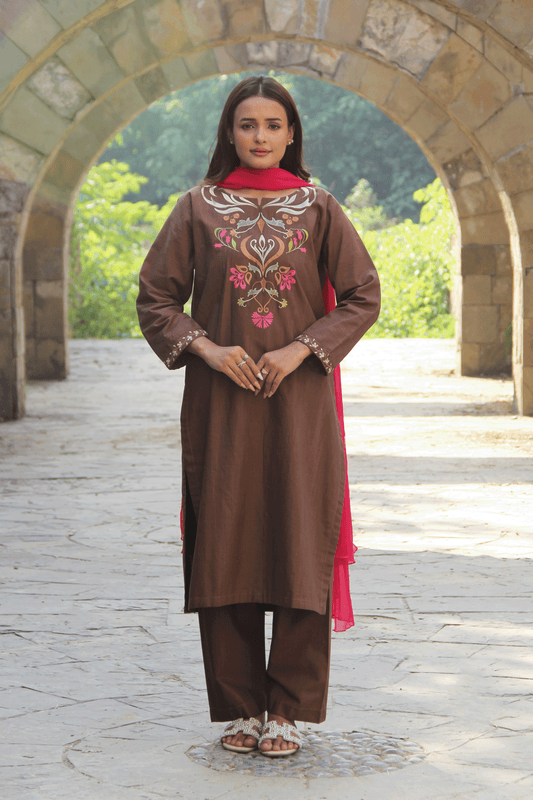 Woman wearing a brown embroidered outfit with a red dupatta in an outdoor setting.