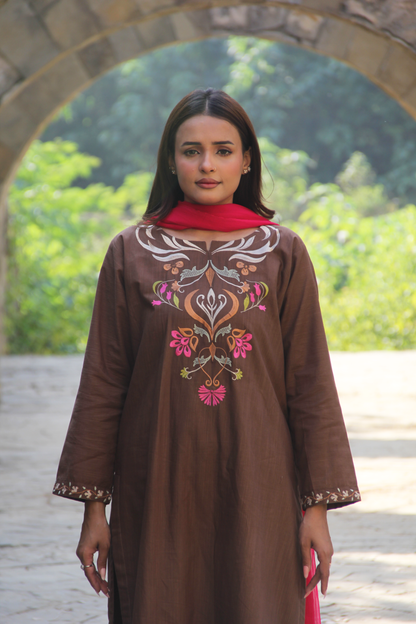 Woman wearing a brown embroidered dress with a red scarf in an outdoor setting