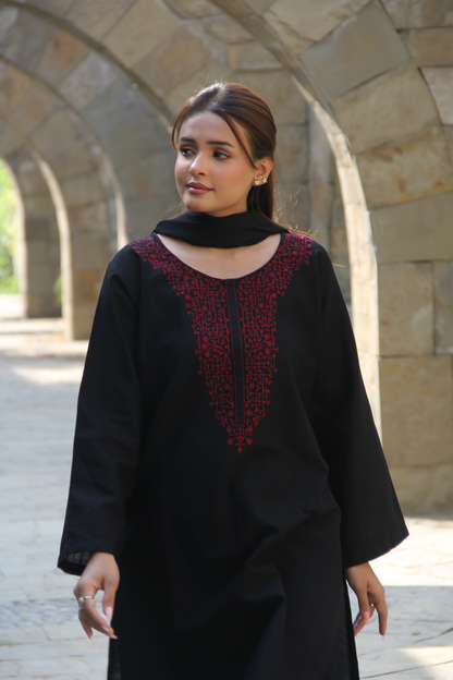 Woman wearing a black outfit with red embroidery in an outdoor setting