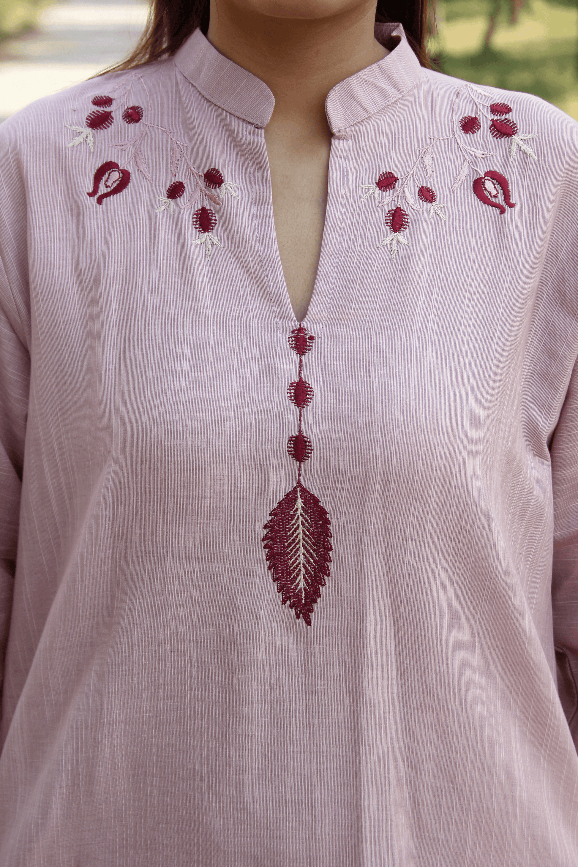 Light pink shirt with red floral embroidery on a blurred natural background