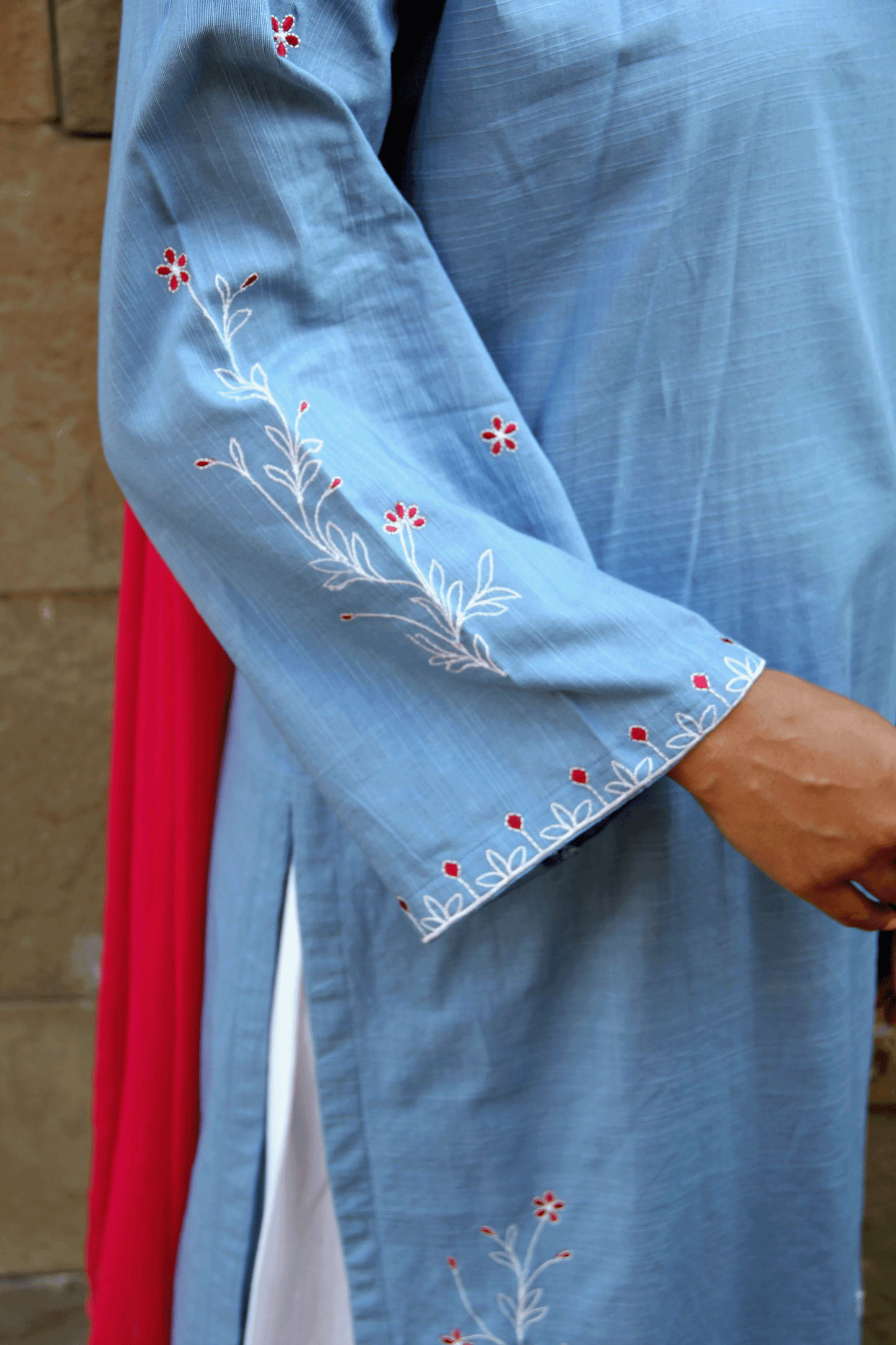 Light blue garment with floral embroidery held by a person against a neutral background
