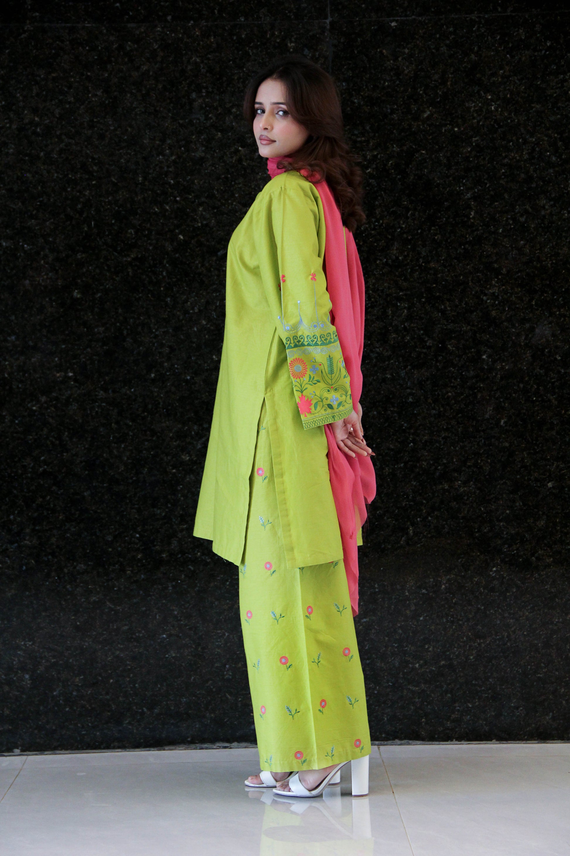Woman wearing a bright green outfit with floral patterns against a black background