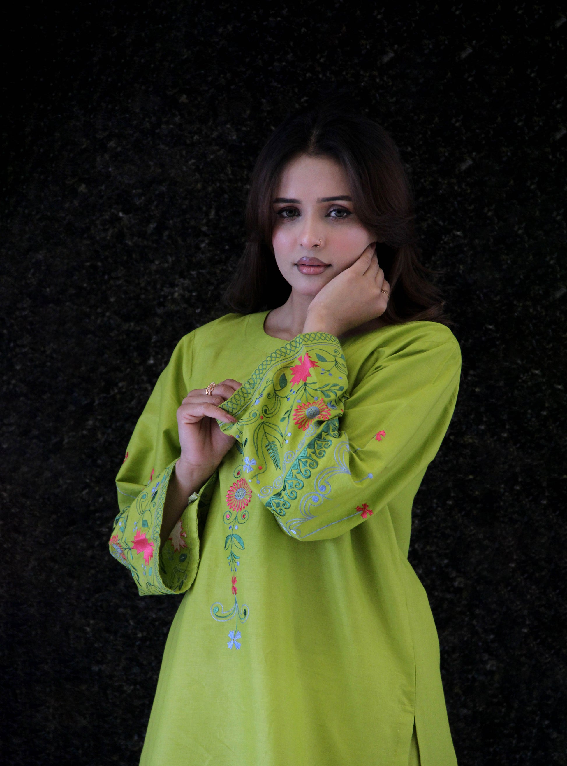 Woman wearing a green embroidered dress against a black background