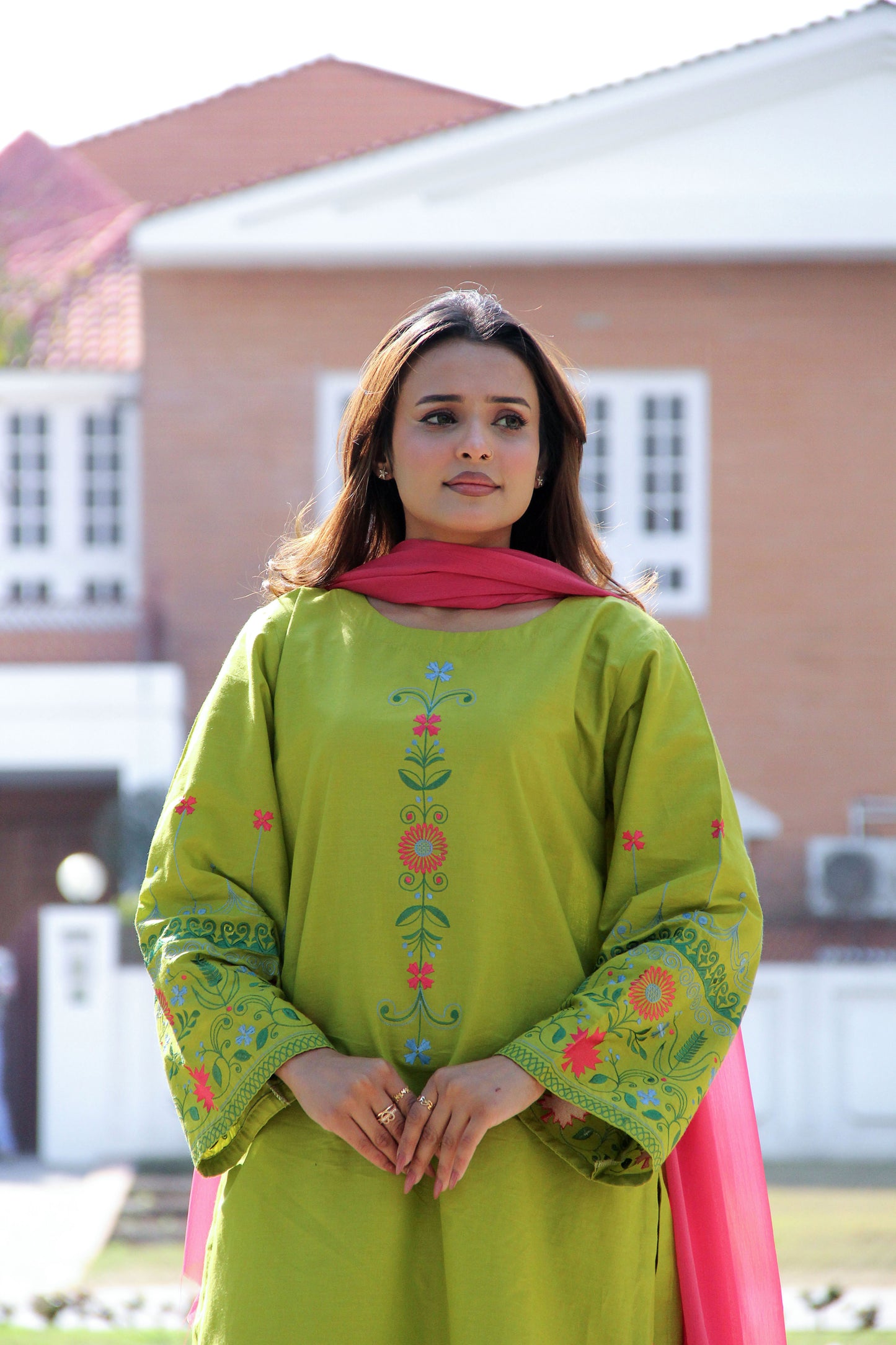 Woman wearing a green embroidered outfit with a pink dupatta outdoors.