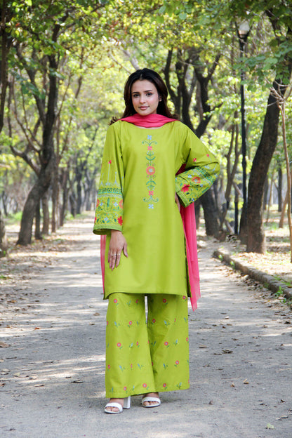 Woman in a green traditional outfit with pink dupatta standing on a path in a park.