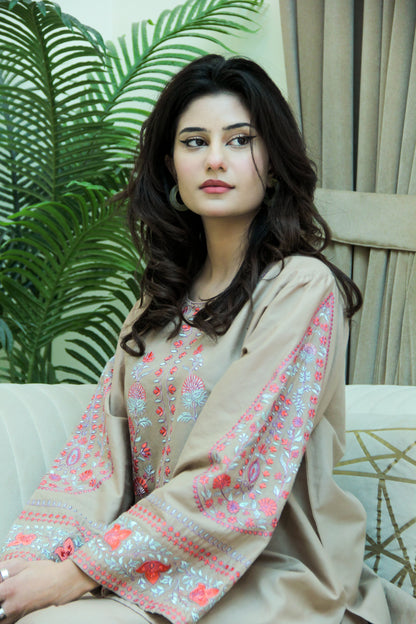Woman wearing a beige embroidered outfit sitting on a couch with a plant in the background