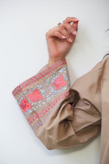 Close-up of a hand wearing a beige sleeve with pink floral embroidery on a white background