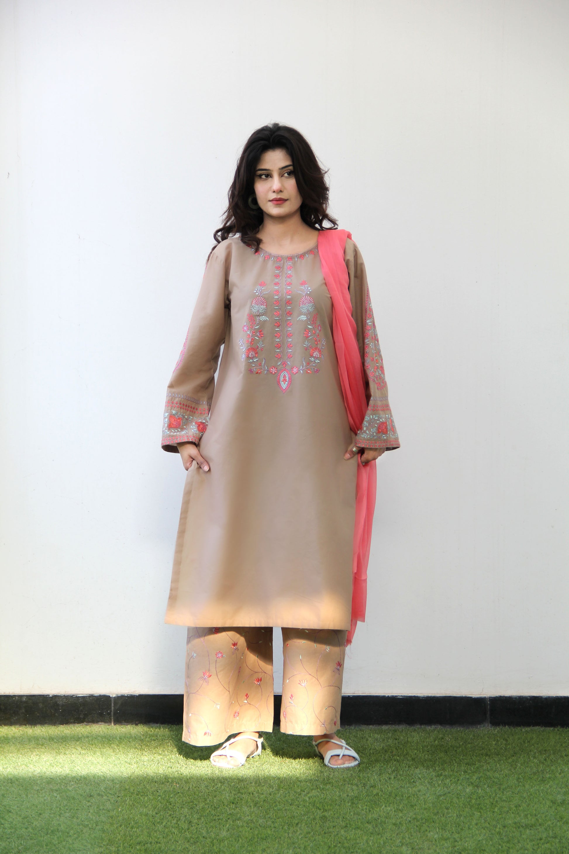 Woman wearing a beige kurta with pink accents against a white wall.
